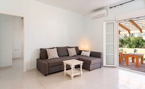 A modern living room with a grey sofa, a small white side table, and a glass door leading to an outdoor area.