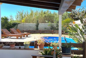 A covered outdoor area with a pool, lounge chairs, and potted plants.