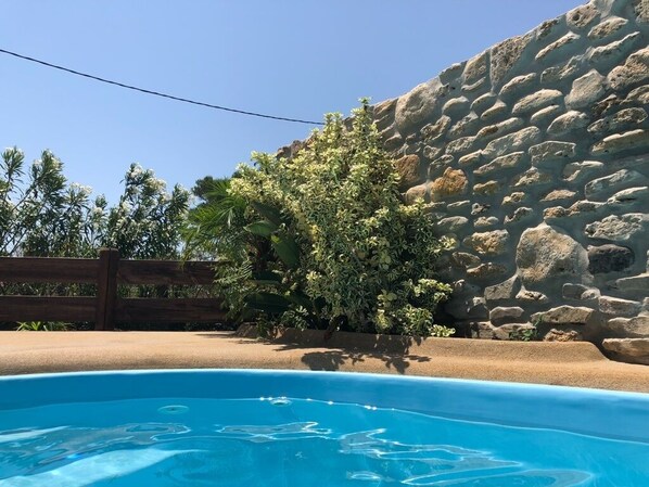 A swimming pool with a stone wall and a wooden fence in the background.
