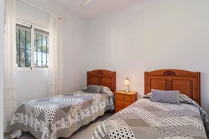 A bedroom with two single beds, a nightstand with a lamp, and a window with curtains.