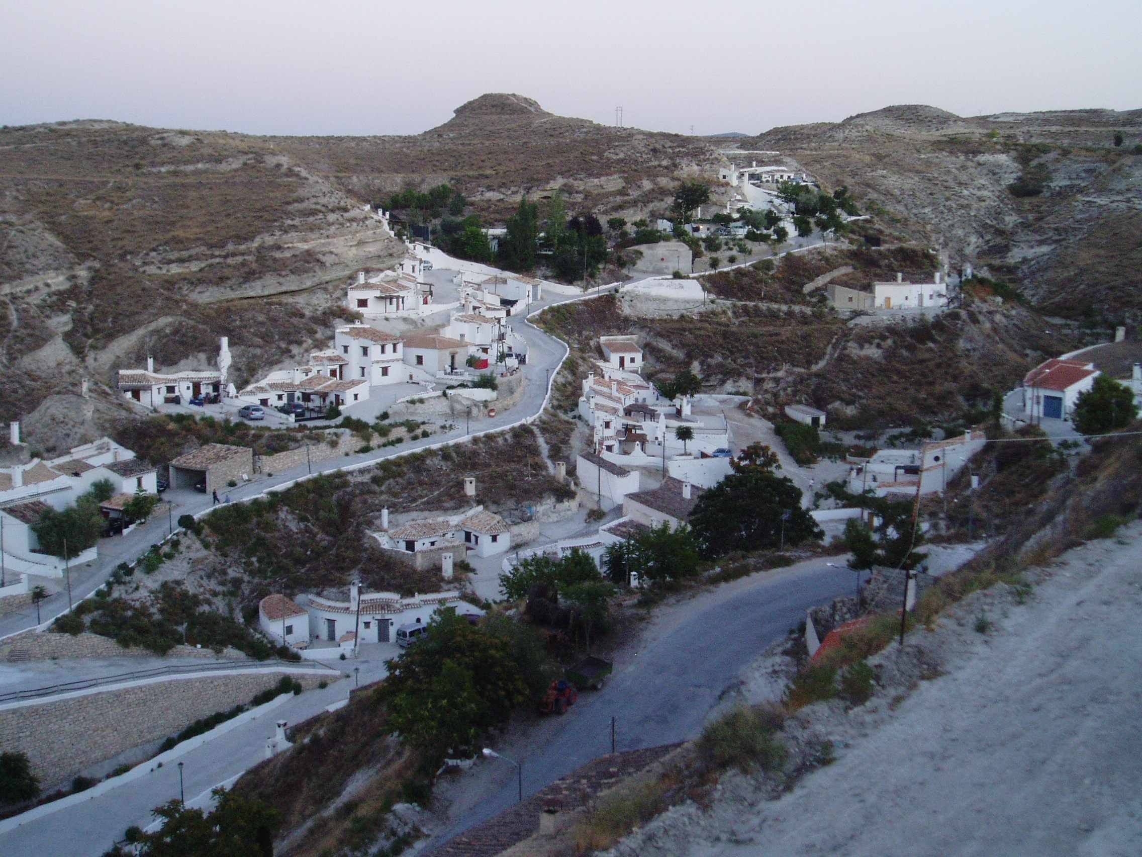 A hillside village with white buildings, narrow winding roads, and rocky terrain.