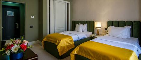 Ein Hotelzimmer mit zwei Betten, einem Schreibtisch mit Blumenvase und einer Tür mit Lampe darüber.