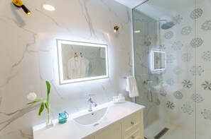 A modern bathroom with a marble wall, a large mirror, a white sink, and a shower area. - Lido by Phoenicia (Bucharest)