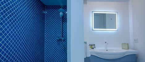 A bathroom with a blue tiled shower, a white sink with a mirror, and a vanity with drawers.