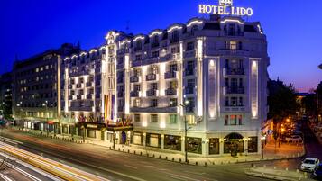 A multi-story hotel with a prominent 'HOTEL LIDO' sign, featuring balconies and a row of shops at the ground level.