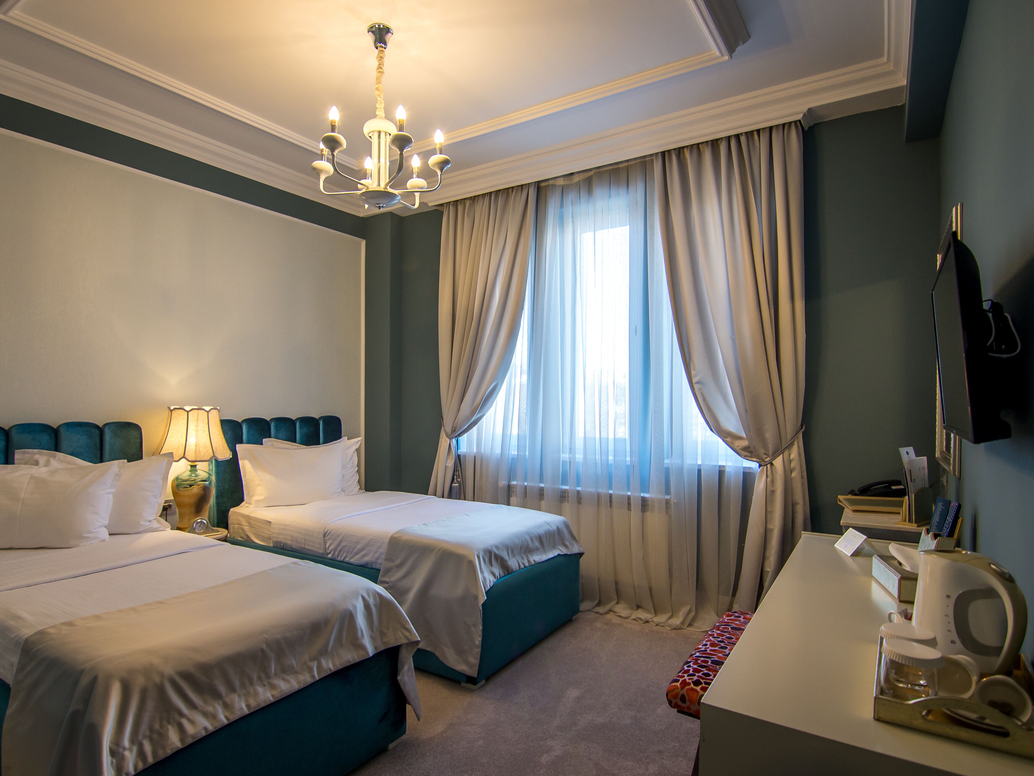 Habitación de hotel con dos camas, un escritorio con teléfono y cafetera, un televisor montado en la pared y una ventana con cortinas.