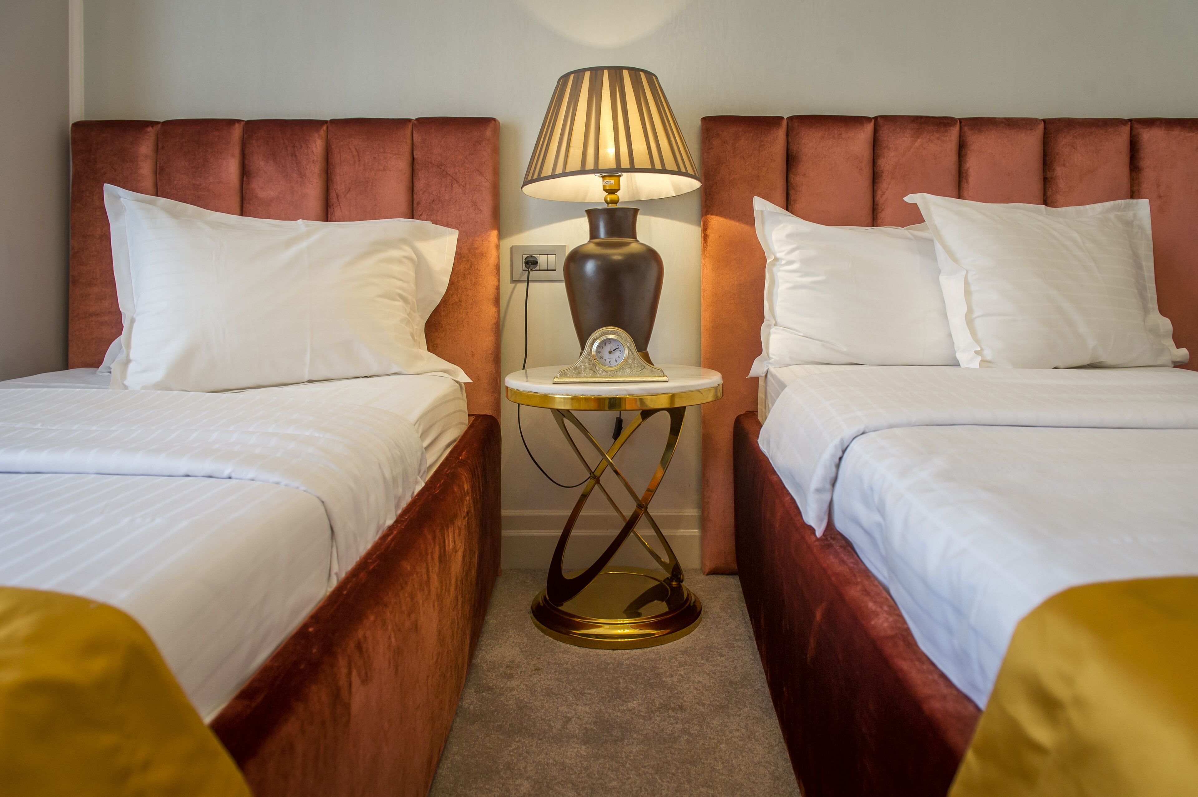A hotel room with two beds, a nightstand with a lamp, and a wall clock.