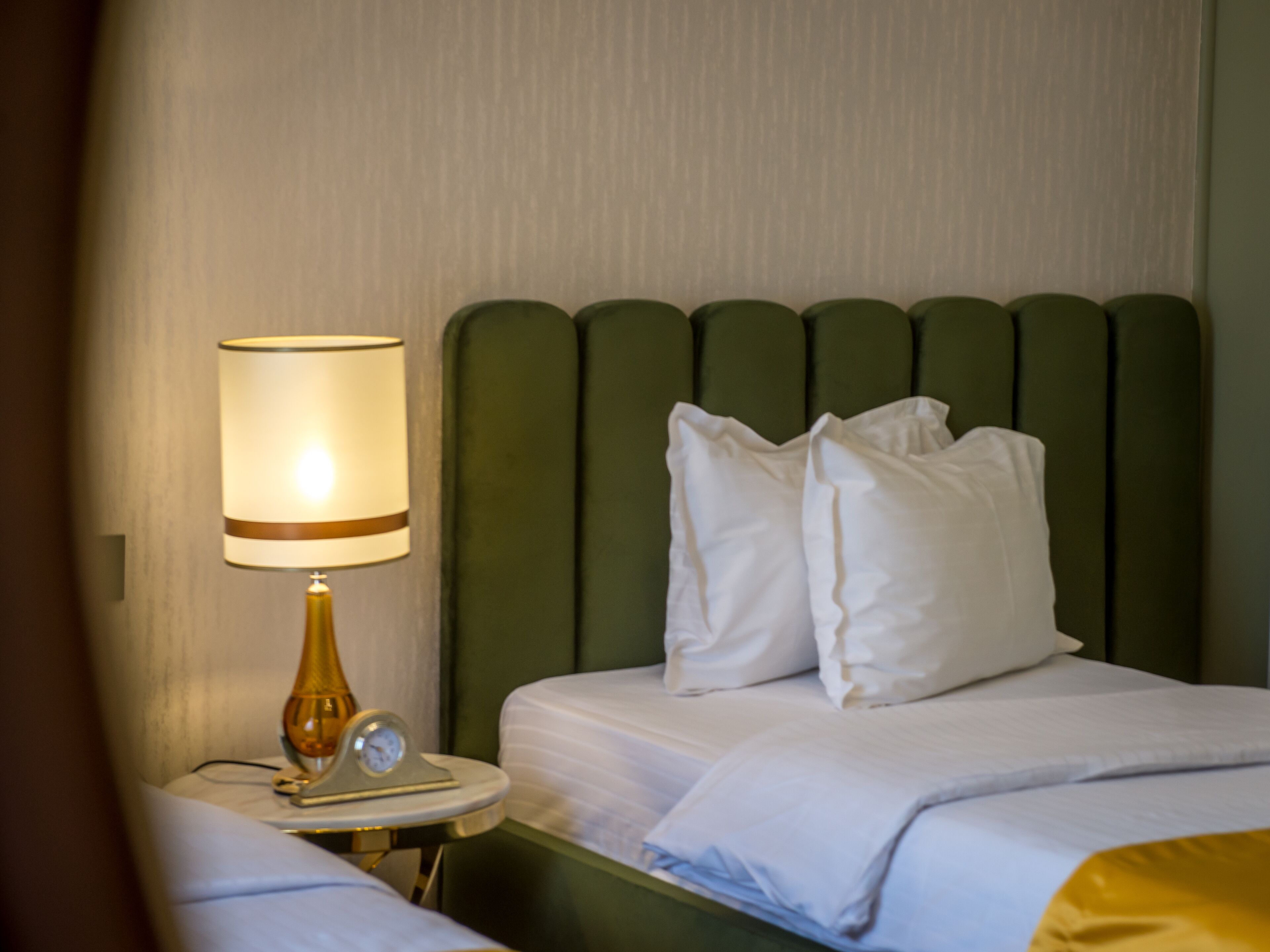 A hotel room with a bed, a bedside table with a lamp, and a clock.