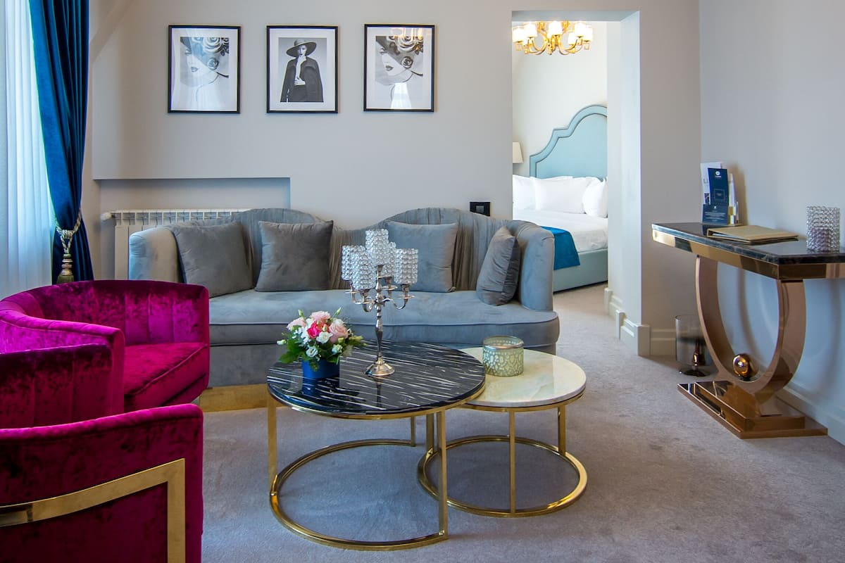 Ein modernes Wohnzimmer mit einem grauen Sofa, einem leuchtend rosafarbenen Sessel, einem runden Couchtisch und einer Kristallleuchter.