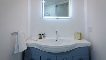 A bathroom with a white sink, a mirror with integrated lighting, and a towel hanging on a rack.