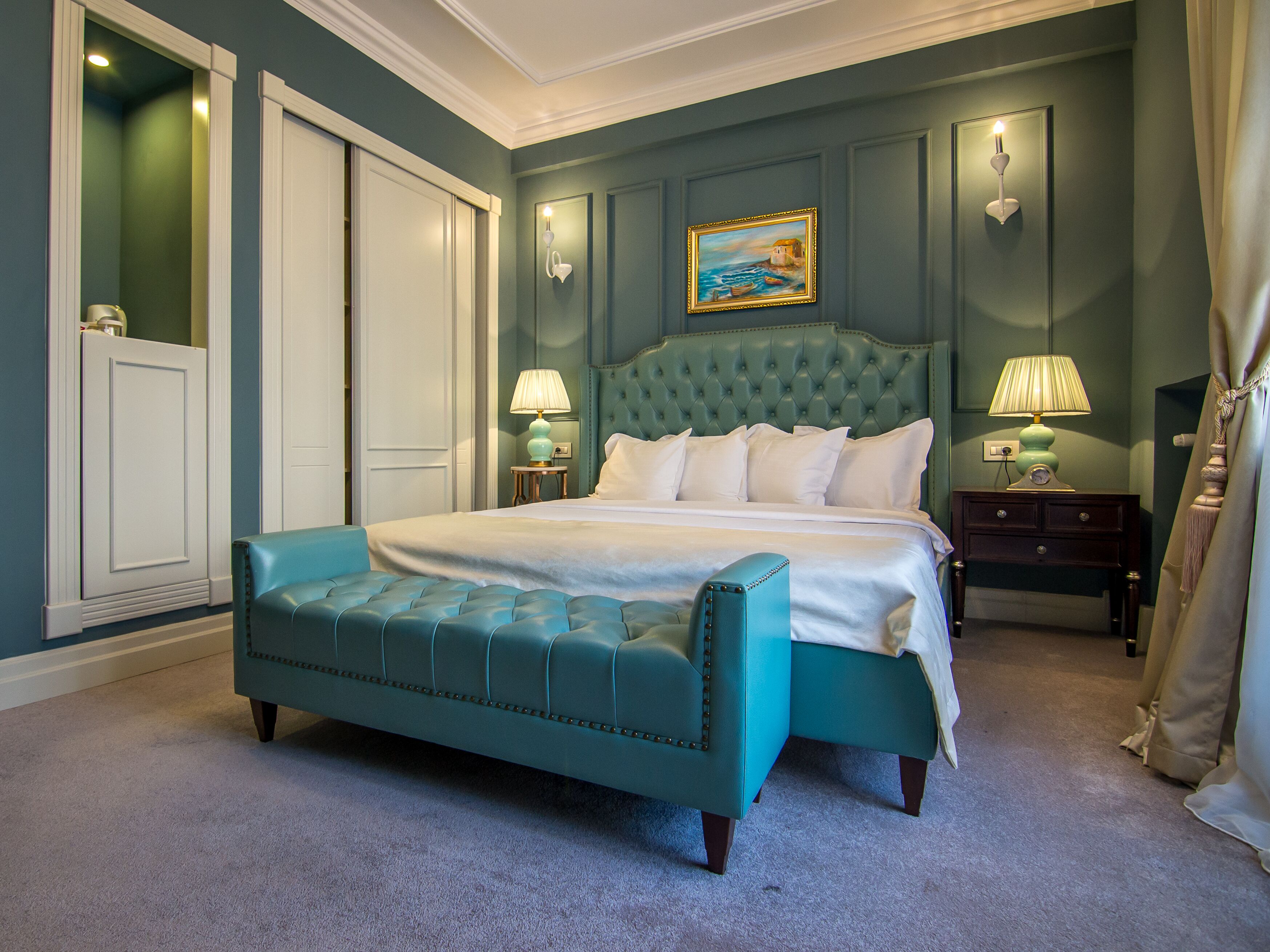 A bedroom with a teal upholstered bed, a tufted headboard, white bedding, and two bedside lamps.