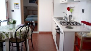 Une cuisine de taille réduite avec un coin repas, des meubles blancs et un sol carrelé.