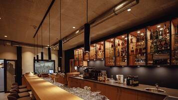 A modern bar area with a long wooden counter, shelves of liquor bottles, and a television screen.