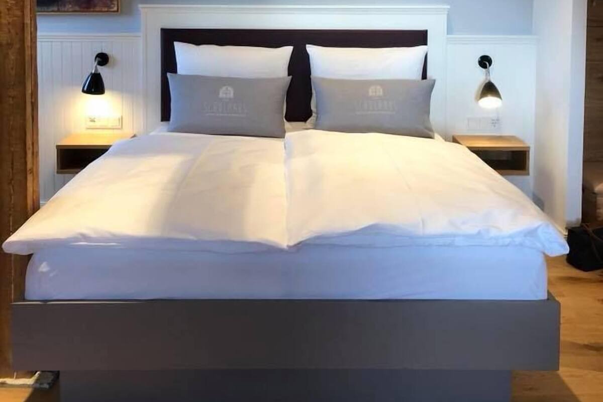 Uma cama com roupa de cama branca, duas mesas de cabeceira com abajures e um painel de cabeceira.