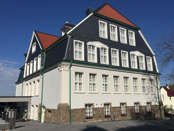 A large, historic building with a symmetrical facade, multiple windows, and a steeply pitched roof.