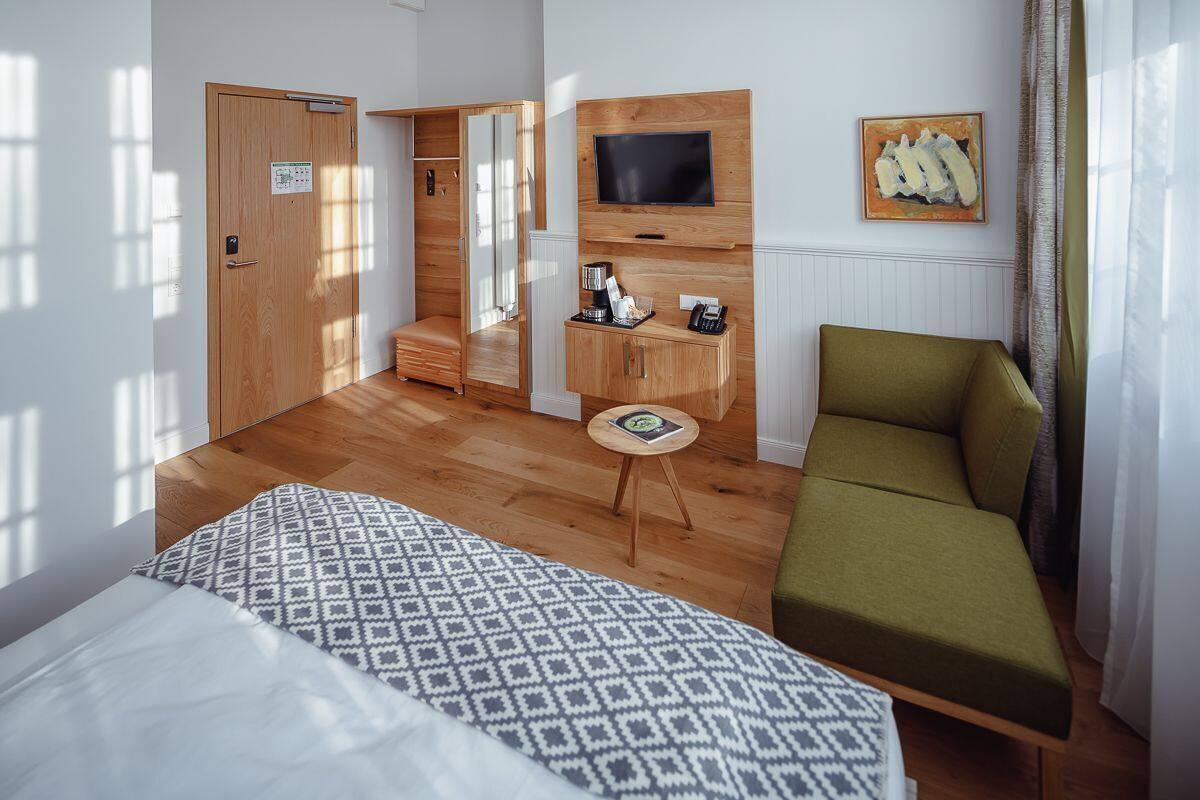 Quarto de hotel com cama, sofá verde, televisão presa na parede, mesa pequena e guarda-roupa.