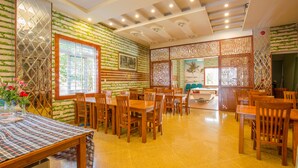 A restaurant with wooden tables and chairs, a large window, and a decorative wall with greenery. - Seika Hotel (Ho Chi Minh City)