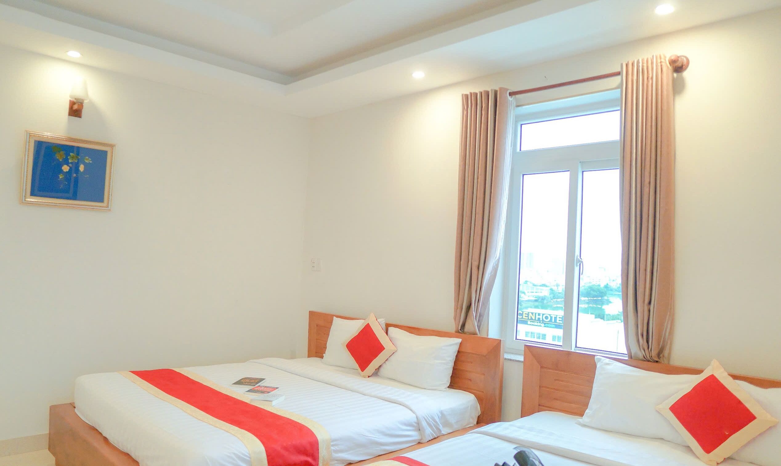 A hotel room with two beds, a window with curtains, a framed picture on the wall, and a view of the city.