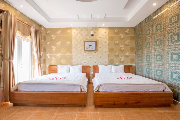 A hotel room with two wooden beds, a large window with curtains, a patterned wall, and a framed picture on the wall.