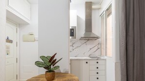 A compact kitchen with white cabinets, a marble backsplash, and a stainless steel range hood. A wooden table with a plant is in the center. - Casa Armonía, charming apartment in the centre (Málaga)