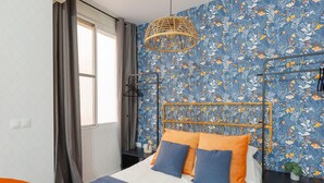 A bedroom with a bed, a hanging light fixture, and a floral-patterned wall. - Casa Armonía, charming apartment in the centre (Málaga)