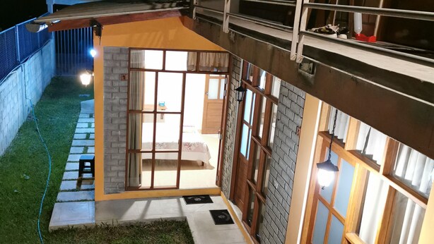 Espaço exterior bem iluminado com área de estar coberta, uma pequena escadaria e vista para o cômodo adjacente.
