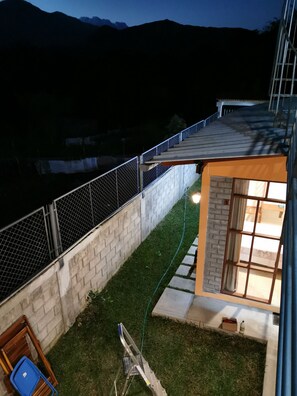 Un patio trasero con terraza de madera, pared de ladrillo y valla metálica.
