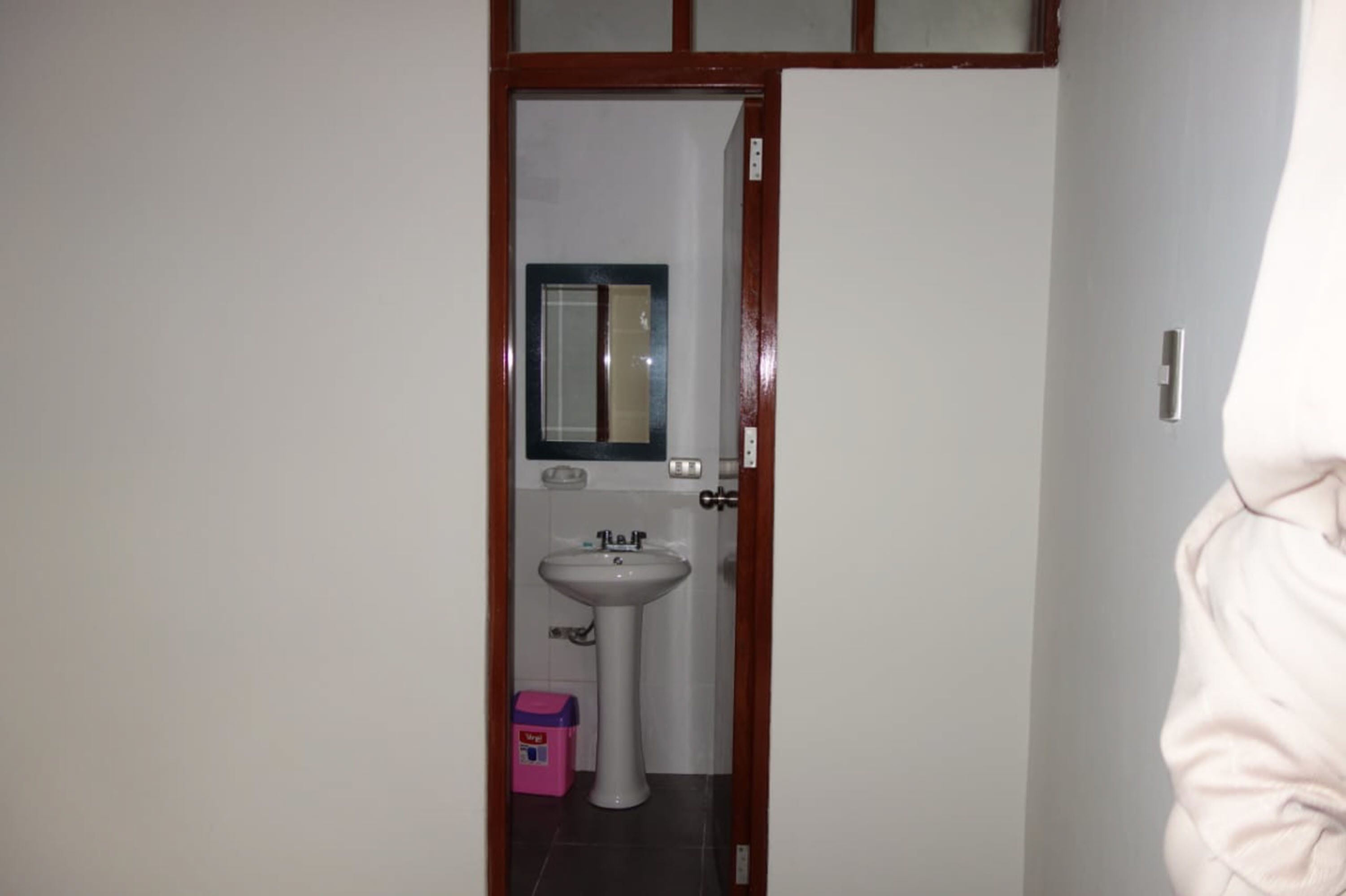 Ein Badezimmer mit einem weißen Waschbecken, einem Spiegel und einer Tür mit Holzrahmen.