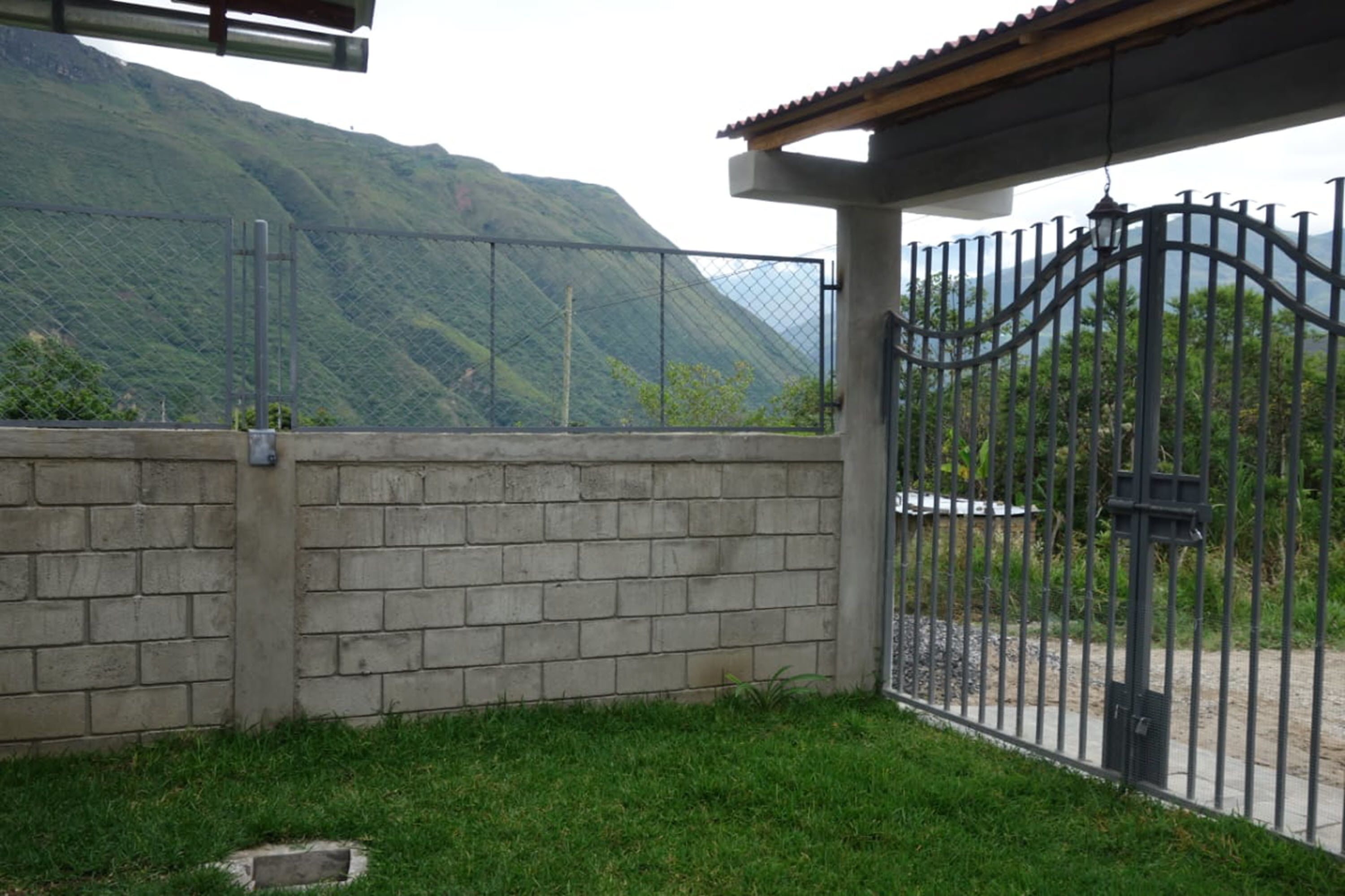 A gated area with a brick wall and a metal gate, overlooking a mountainous landscape.