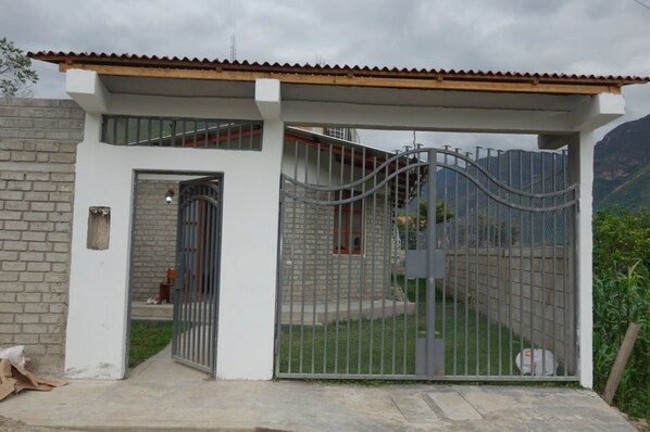 Una propiedad residencial privada con reja, fachada blanca, puerta metálica y un pequeño porche.