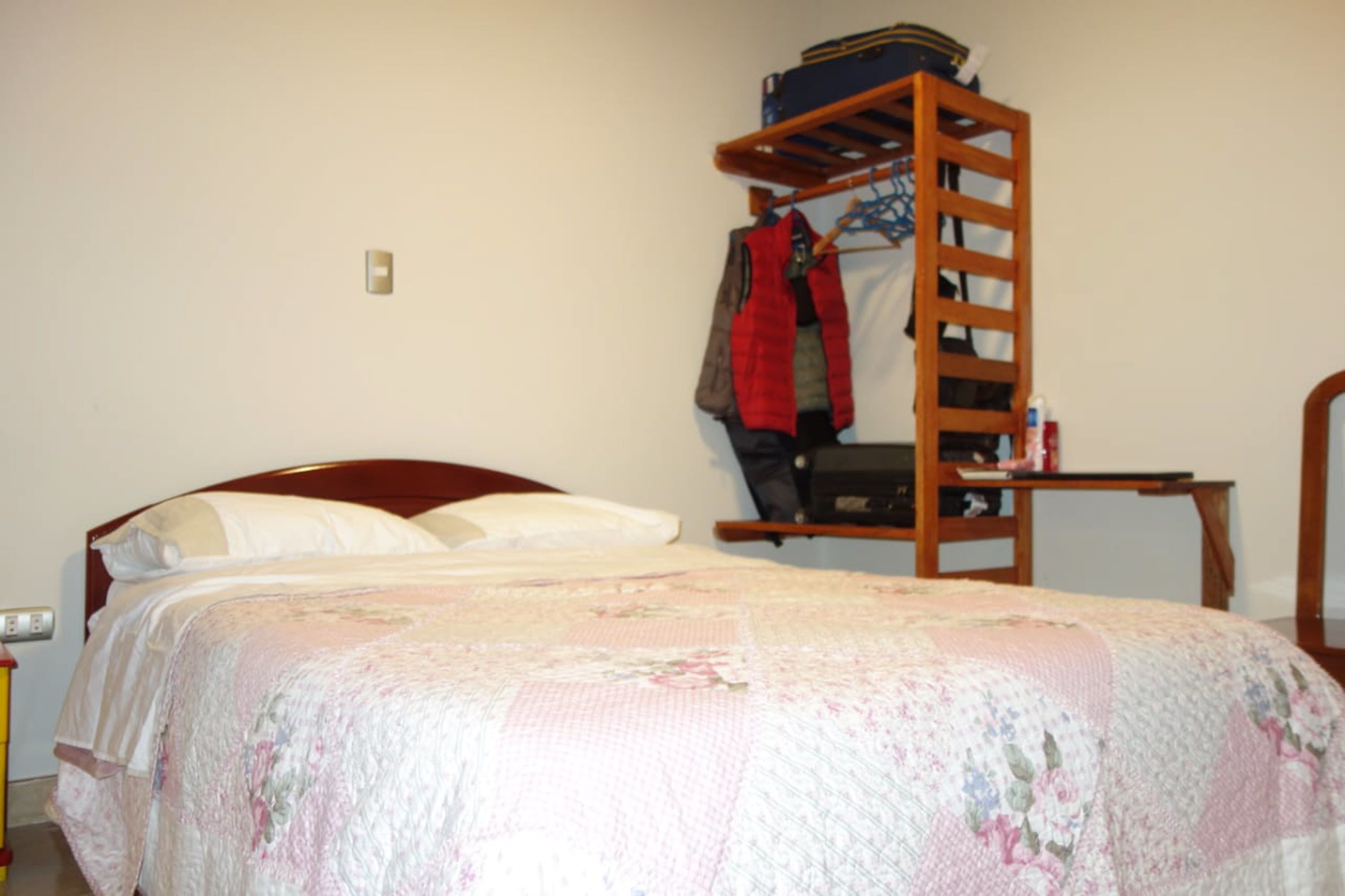 A bedroom with a wooden bunk bed, a single bed with a floral comforter, and a small table with a chair.