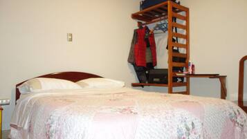 A bedroom with a wooden bunk bed, a single bed with a floral comforter, and a small table with a chair.