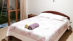 Quarto com cama, cabeceira de madeira, mesa de cabeceira, prateleira na parede e porta de vidro deslizante para área externa.