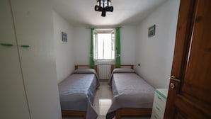 Ein Schlafzimmer mit zwei Einzelbetten, einer Holzkommode, einem Heizkörper und einem Fenster mit grünen Vorhängen.