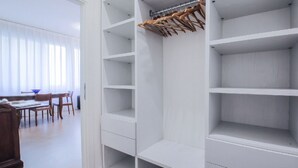 Une pièce avec une armoire blanche, une table à manger avec des chaises et une fenêtre ornée de rideaux légers.