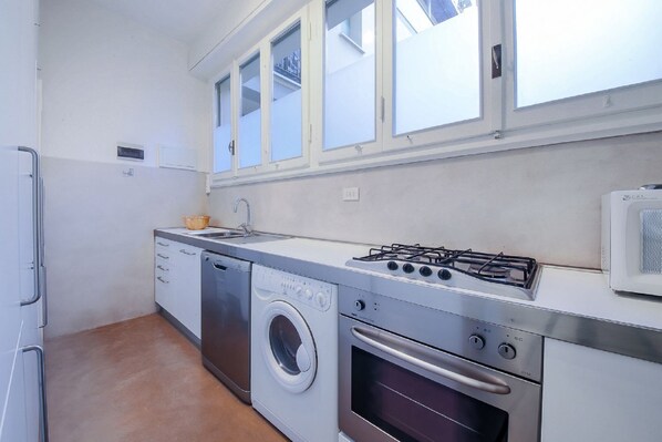 A compact kitchen with a washing machine, oven, gas stove, and a microwave.