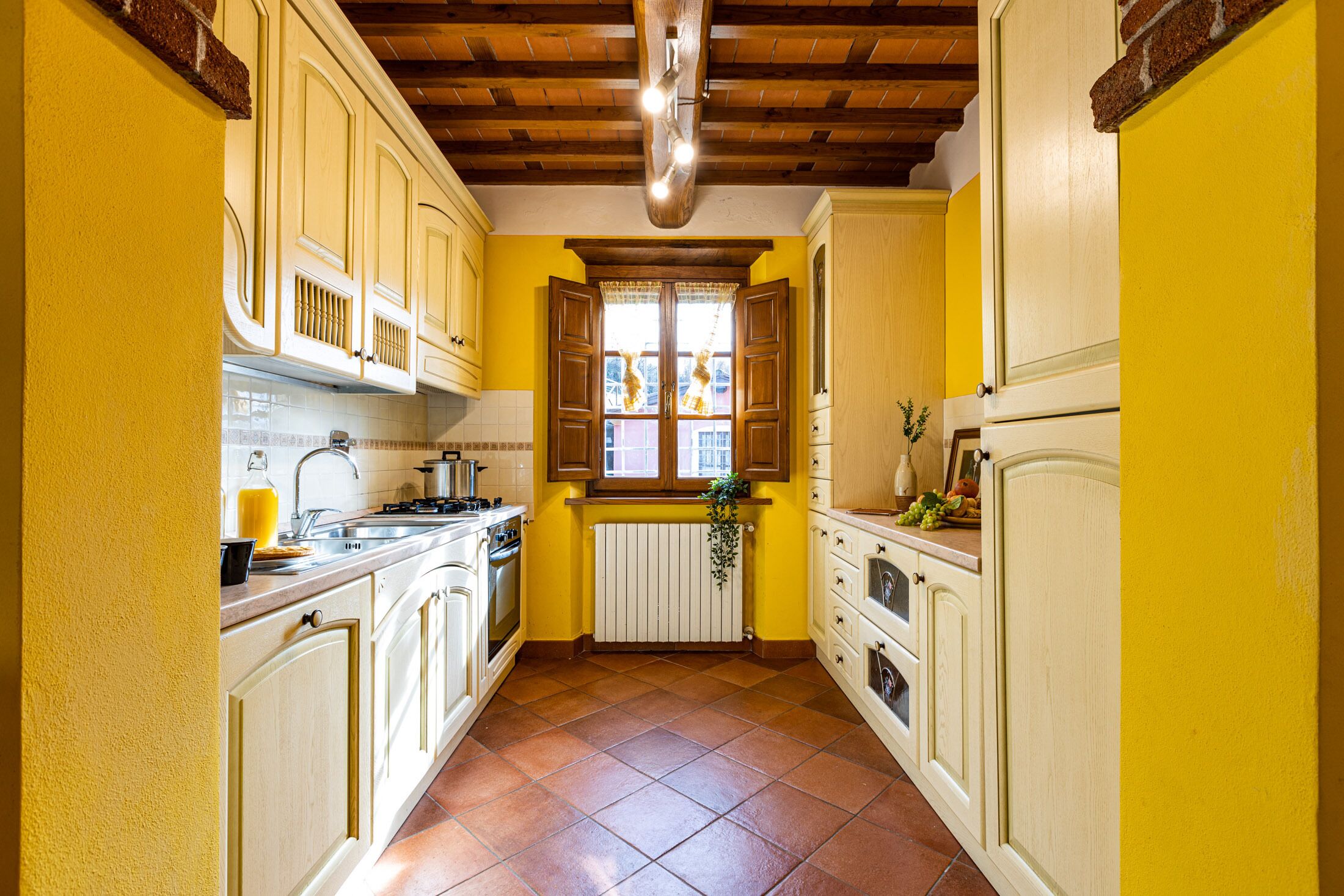 A narrow kitchen with yellow walls, wooden cabinets, and a tiled floor.