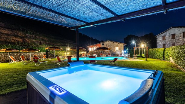 A hot tub under a covered area with a pool in the background.