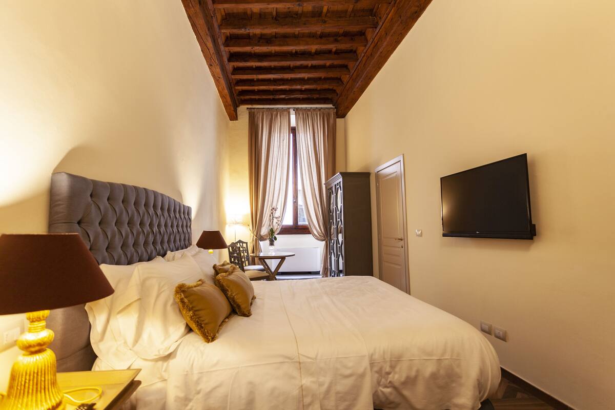 Een hotelkamer met een groot bed, een flatscreen televisie, een houten plafond en een raam met gordijnen.