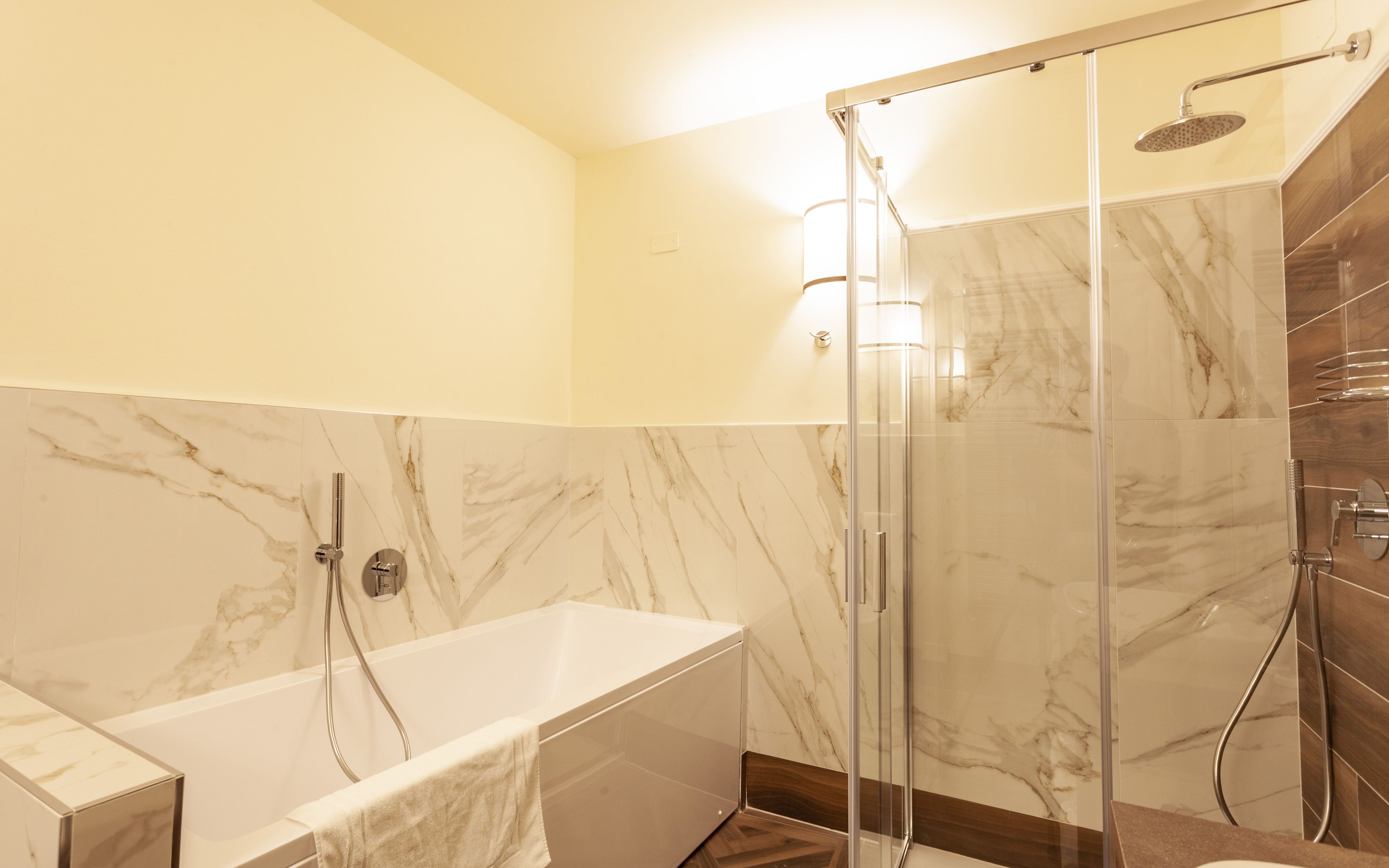 A modern bathroom with a glass-enclosed shower, a standalone bathtub, and marble walls.