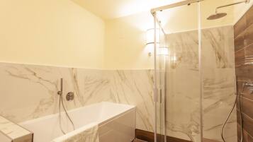 A modern bathroom with a glass-enclosed shower, a standalone bathtub, and marble walls.