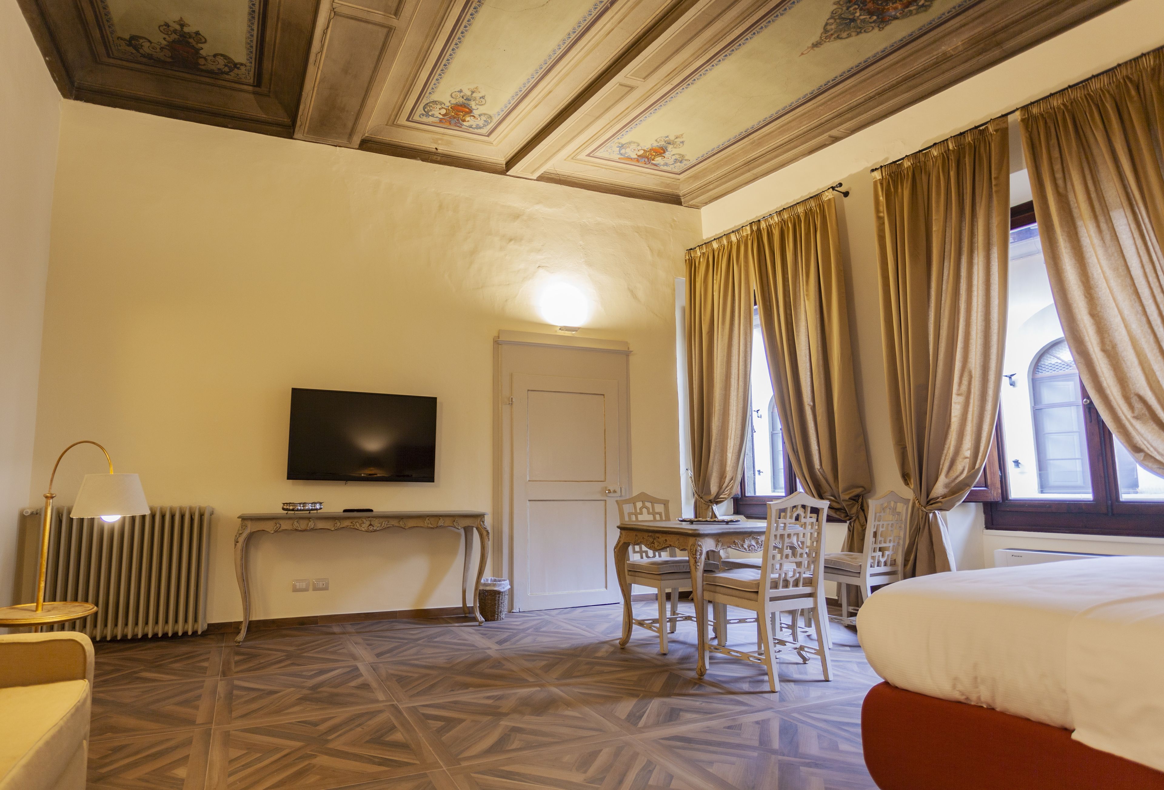 A hotel room with a television, a dining table with chairs, a bed, and a radiator.