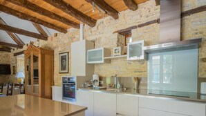 A modern kitchen with stone walls, wooden beams, a built-in oven, and a large refrigerator.
