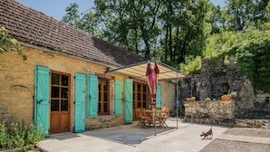 A rustic stone building with a tiled roof, wooden shutters, and a patio area with outdoor seating.