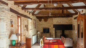A rustic room with stone walls, wooden beams, a large table with a red tablecloth, a television, and a cabinet.