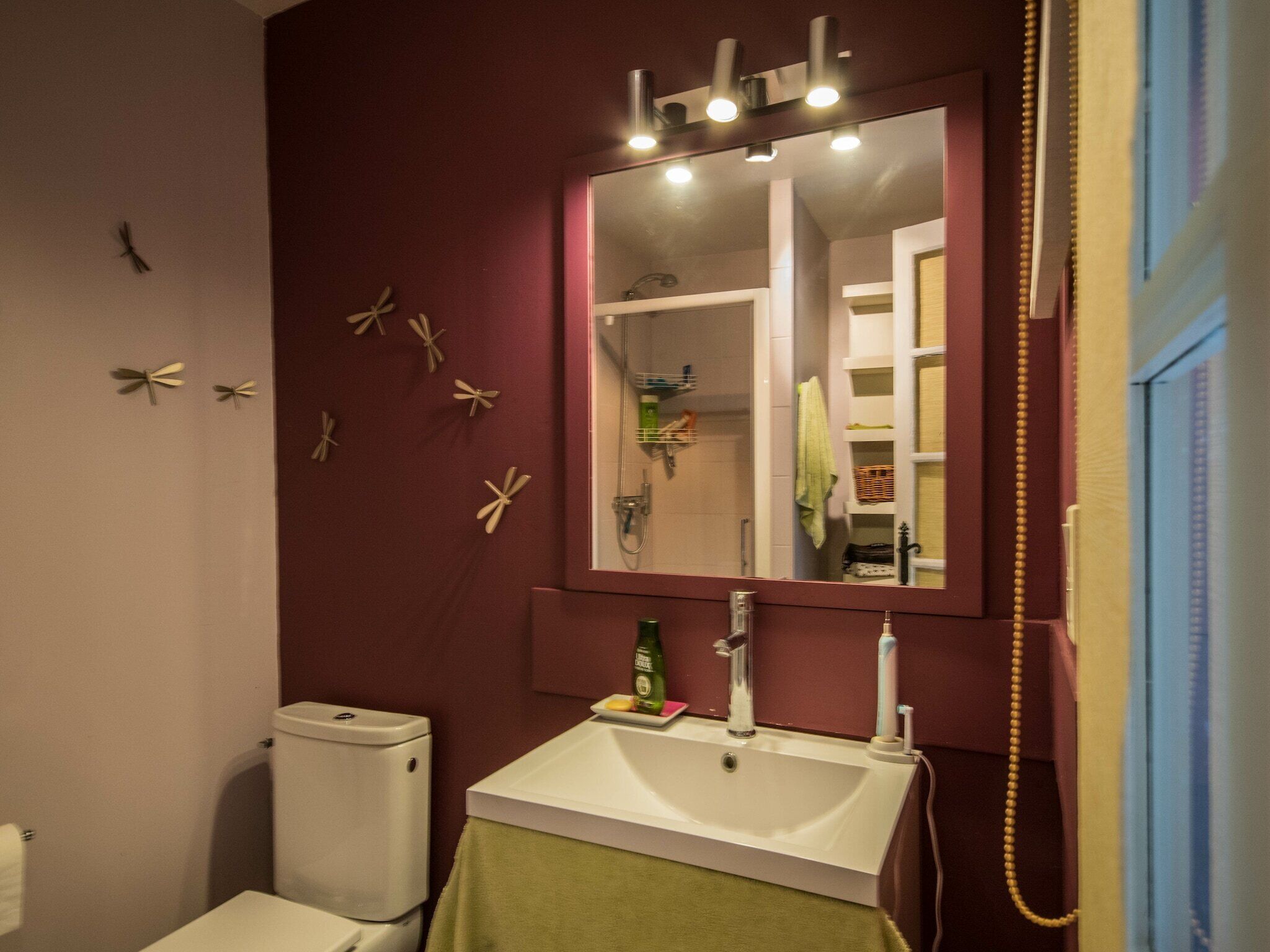 Une salle de bain avec un lavabo blanc, un miroir au-dessus et des toilettes. Des étoiles de mer décoratives sont accrochées au mur.