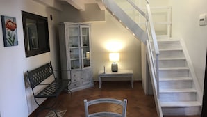 Eine Treppe führt zu einer oberen Etage, ein Essbereich mit Tisch und Stühlen, eine Vitrine mit Glastüren und eine Wandleuchte.