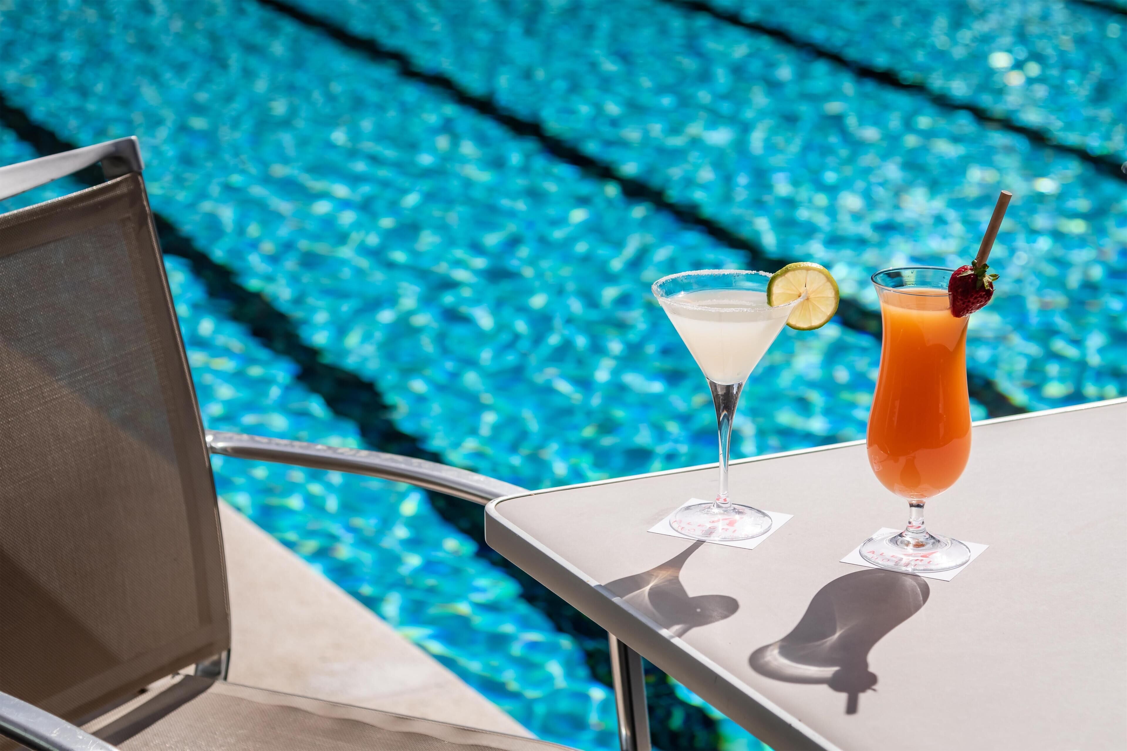 Mesa junto a la piscina con dos bebidas, una con rodaja de limón y la otra adornada con fresa.