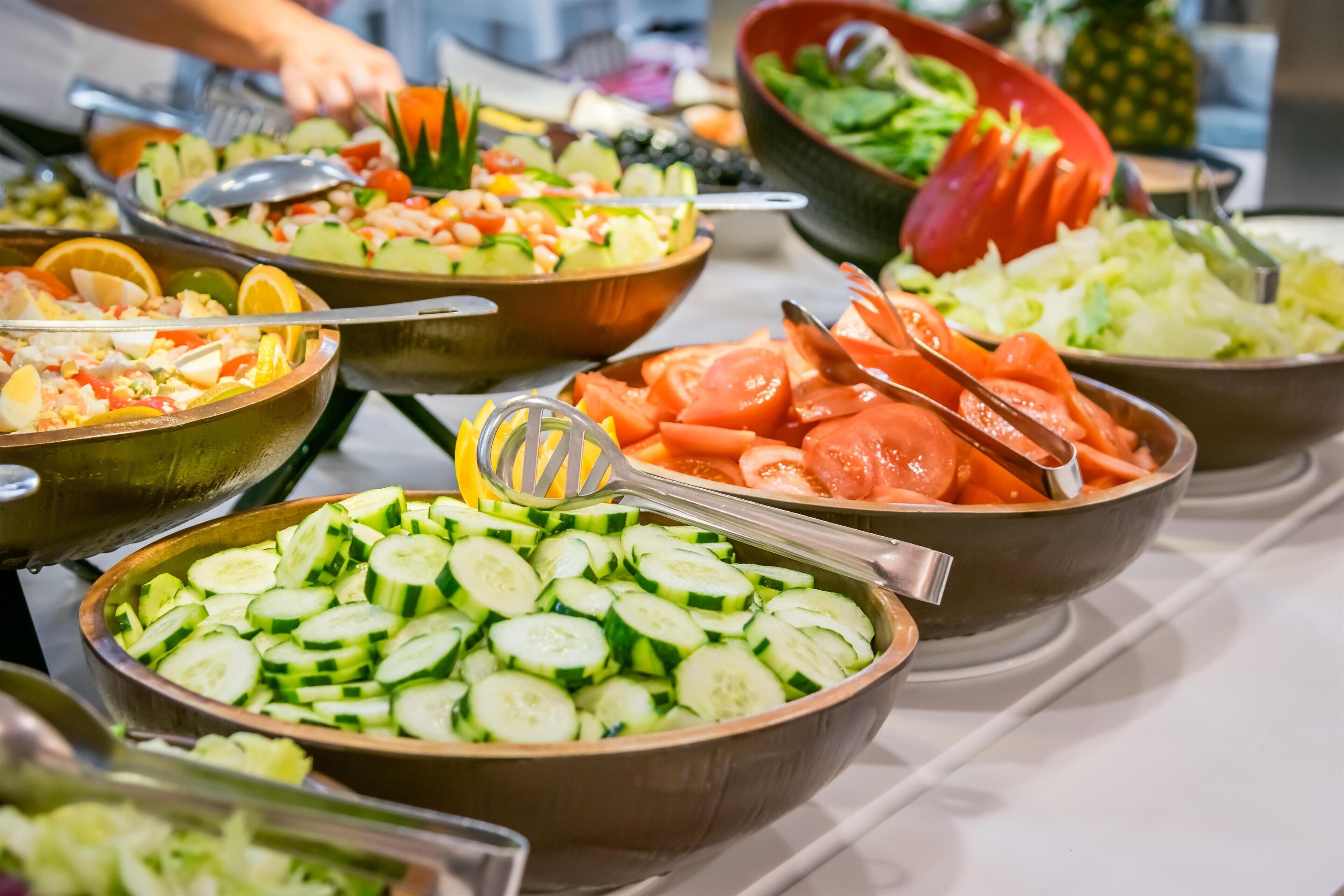 Un bufé con diversas opciones de comida, incluyendo ensaladas, frutas y verduras.