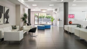 A modern hotel lobby with white sofas, a blue ottoman, and a large potted plant. - ALEGRIA Mariner - Adults Only (Lloret de Mar)